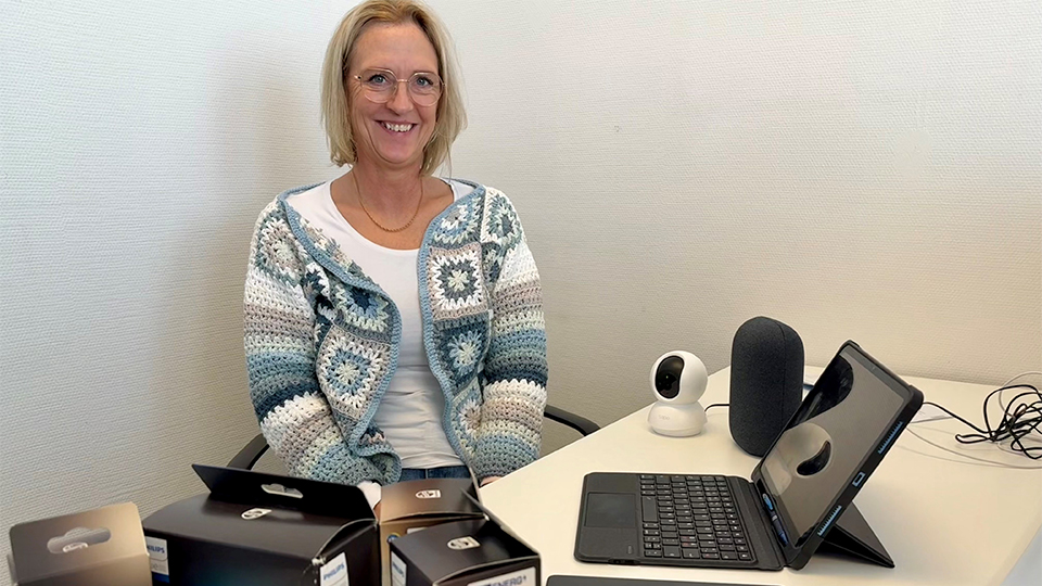 Cecilia Öhman sitter vid ett skrivbord där det ligger kartonger med belysning, surfplattor, kameror och andra prylar.
