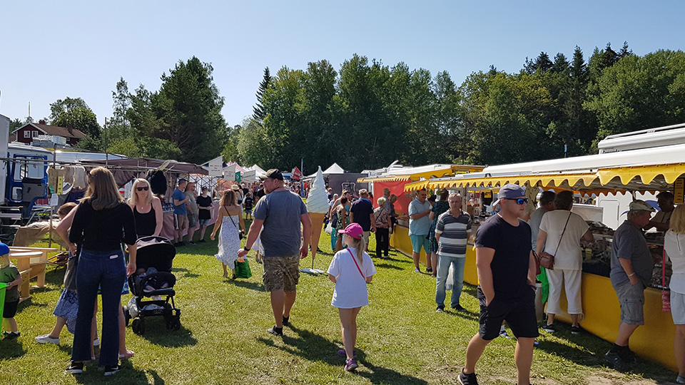 En solig sommardag med många bord uppställda på gräset. Här säljs allt möjligt och folk vandrar mellan borden.